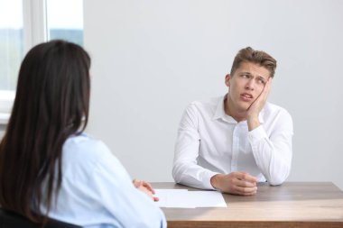 Ahşap masada oturan genç bir adam kadınlara şikayette bulunuyor.