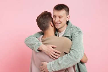 Pembe arka planda sarılan iki mutlu arkadaş.