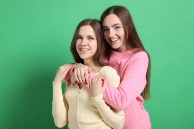 Arkadaşlar yeşil arka planda birbirlerine sarılıyorlar.