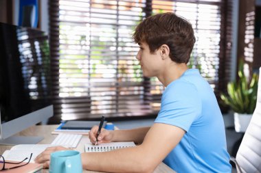 Ergen öğrenci içeride çalışırken bilgisayar kullanıyor.