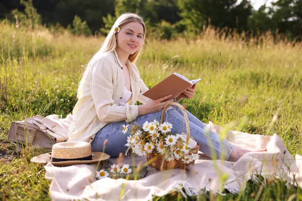 Bir buket kır çiçeğiyle çayırda kitap okuyan bir kadın.