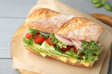 Gri ahşap masada jambonlu, peynirli ve sebzeli lezzetli baget sandviç.