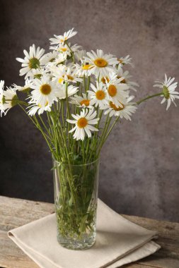 Tahta masadaki vazoda, kahverengi desenli arka planda birçok güzel papatya çiçeği, yakın plan.