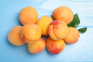 Açık mavi ahşap masa üzerinde yeşil yapraklı taze kayısılar.