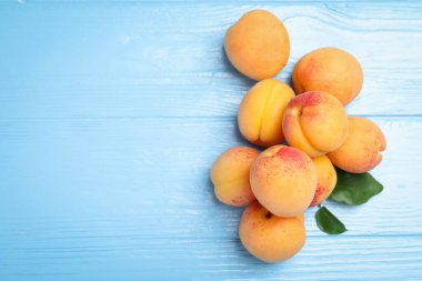 Açık mavi ahşap masa üzerinde yeşil yapraklı taze kayısılar. Metin için boşluk