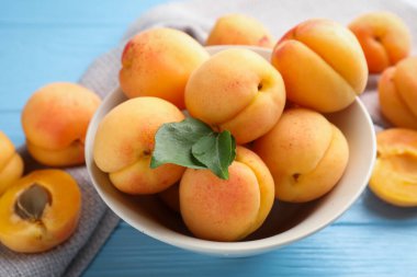 Açık mavi ahşap masada yeşil yapraklı taze kayısılar, yakın plan.