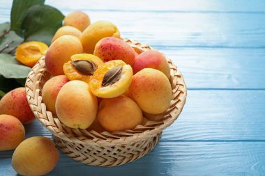 Hasır sepetteki taze kayısılar açık mavi ahşap masada, yakın plan.