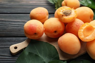 Taze kayısılar ve yeşil yapraklar koyu ahşap masada, yakın plan.