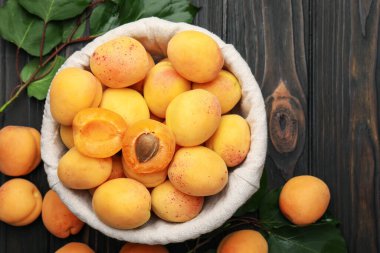 Taze kayısılar ve yeşil yapraklar koyu ahşap masada, düz yatıyordu.