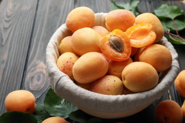 Sepette taze kayısılar ve ahşap masada yeşil yapraklar, yakın plan.