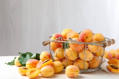 Taze kayısılar metal sepette ve yeşil yapraklar beyaz ahşap masada.