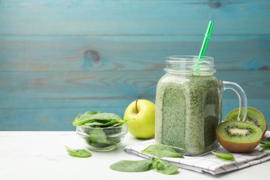 Mason kavanozunda leziz bir smoothie, ıspanak yaprakları, kivi ve elma beyaz masada açık mavi ahşap arka planda, yakın plan. Metin için boşluk