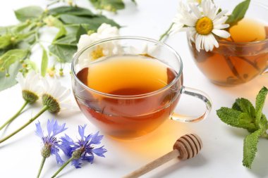 Cam fincanlarda aromatik bitki çayı, farklı çiçekler ve beyaz arkaplanda nane şekeri, yakın plan.