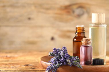 Ahşap masa üzerinde lavanta yağı ve çiçek şişeleri, yakın plan. Metin için boşluk