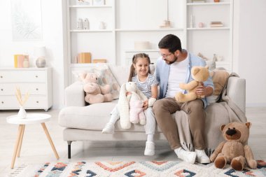 Baba ve kızı evdeki kanepede pelüş hayvanlarla oynuyorlar.