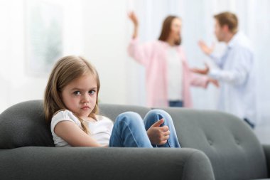 Kanepede üzgün küçük bir kız ve ailesi evde kavga ediyor, seçici bir odaklanma.