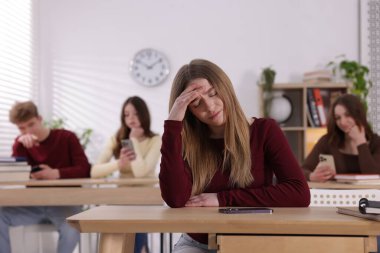 Siber zorbalık. Sınıfta masasında akıllı telefonu olan üzgün bir genç kız.