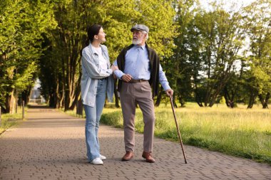 Gülümseyen bakıcı dışarıda bastonuyla yaşlı bir adamı destekliyor.
