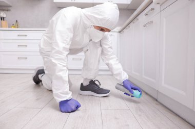 Koruyucu kıyafetli haşereci evde böcek ilacı sıkıyor.