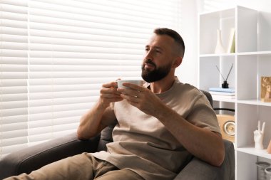 Uyum. Evdeki koltukta içki içen adam.