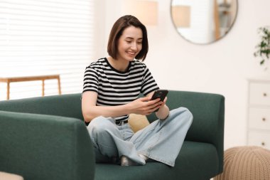 Evdeki koltukta modern akıllı telefon kullanan bir kadın.