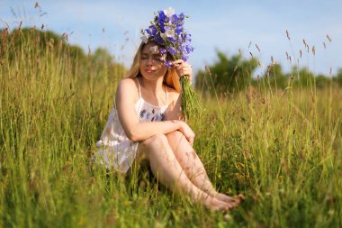 Bir buket kır çiçeğiyle güzel bir kadın çayırda güneşli bir günün tadını çıkarıyor.