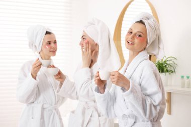 İçerideki spa prosedürlerinden sonra bornozlu ve sağlıklı bir bardak içecekle mutlu kadınlar, seçici bir odak noktası.