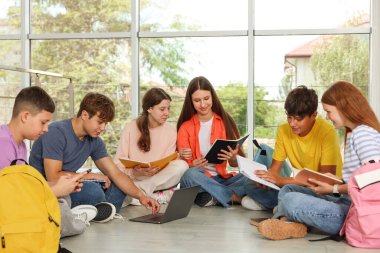 Defterleri ve dizüstü bilgisayarı olan bir grup genç içeride birlikte çalışıyorlar.