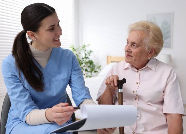 Nurse with clipboard examining senior woman indoors. Home health care service