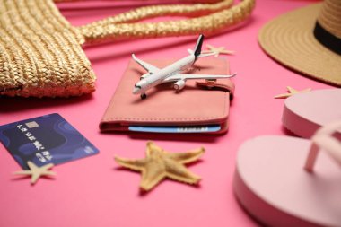 Uçak modeli, pasaport, uçuş bileti, kredi kartı ve pembe arka planda plaj aksesuarları, yakın plan.