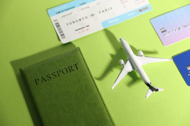 Uçak modeli, uçuş bileti, pasaport ve kredi kartları yeşil arka planda.