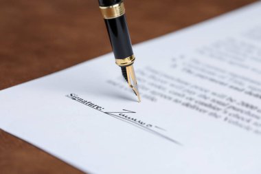 Kahverengi masadaki dolma kalemle noter belgesi imzalanırken, yakın plan