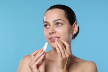 Açık mavi arka planda dudak merhemi olan genç bir kadın.