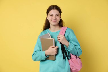 Sırt çantası ve sarı arka plan kitapları olan genç bir kız.