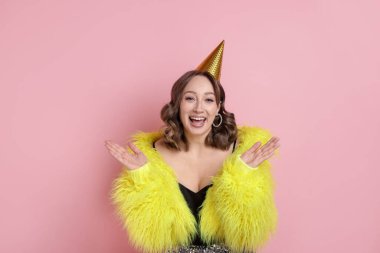 Doğum günü kutlaması. Pembe arka planda parti konisi olan mutlu kadın.