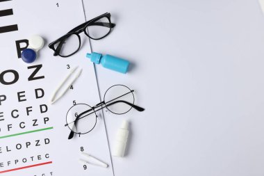 Vizyon testi çizelgesi, gözlük, cımbız, beyaz arka planda tıbbi damlalar ve lensler. Metin için boşluk