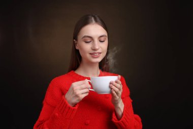 Kahverengi arka planda bir fincan kahveyle gülümseyen kadın.