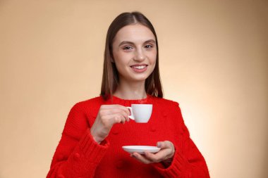 Bej renkli arka planda bir fincan kahveyle gülümseyen kadın