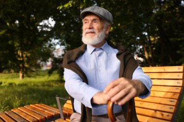 Dışarıda bankta oturan bastonlu yakışıklı yaşlı adam.
