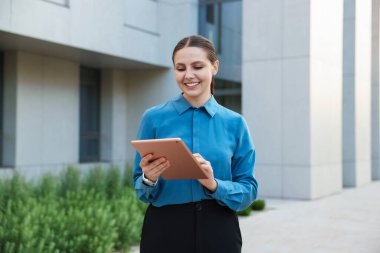 Ofis binasının yakınında tableti olan mutlu bir iş kadını.