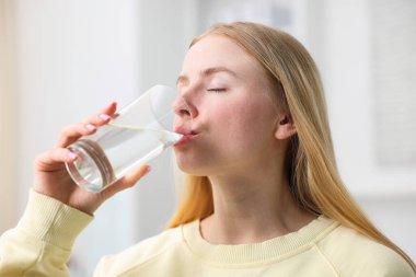 Genç bir kadın evde camdan su içiyor.