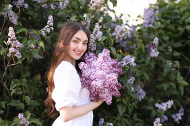 Leylak çiçeklerinin arasında gülümseyen ve açık havada terk eden kadın.