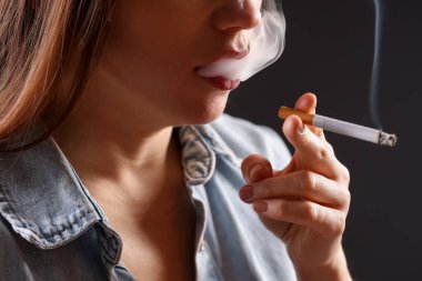 Arka planda sigara içen tişörtlü bir kadın, yakın plan. Kötü alışkanlık.