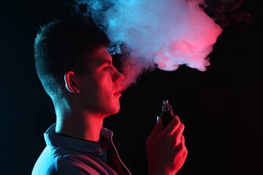 Siyah arkaplanda neon ışıkları altında elektronik sigara içen adam