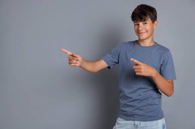 Genç çocuk gri arka planda bir şeye işaret ediyor, mesaj için boşluk