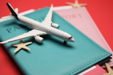 Uçak modeli, pasaportlar, uçuş biletleri ve kırmızı arka planda deniz yıldızları, yakın plan.