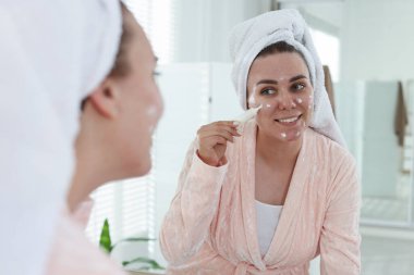 Kadın evin içinde aynanın yanında yüzüne krem sürüyor. Sivilce tedavisi
