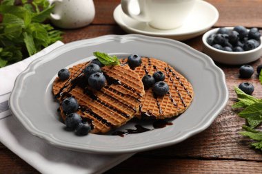 Ahşap masada yaban mersini, nane ve çikolata soslu Lezzetli Hollanda waffleları (stroopwafels).