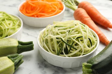 Farklı vejetaryen erişteleri ve beyaz mermer masada taze sebzeler, yakın plan.