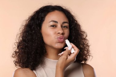 Bej arka planda dudaklarına dudak kremi süren güzel bir kadın.